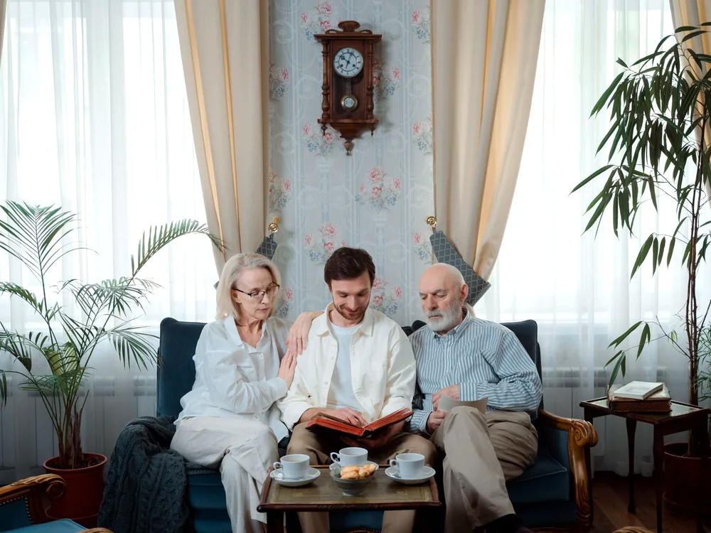 Un couple de seniors partage un album photo avec un proche dans un salon.